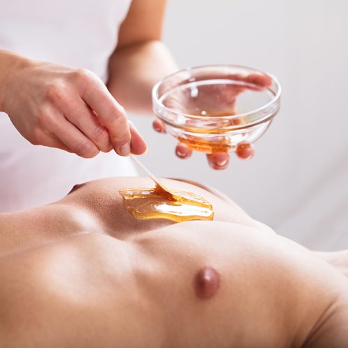 Close-up Of A Therapist Applying Wax On Man's Body